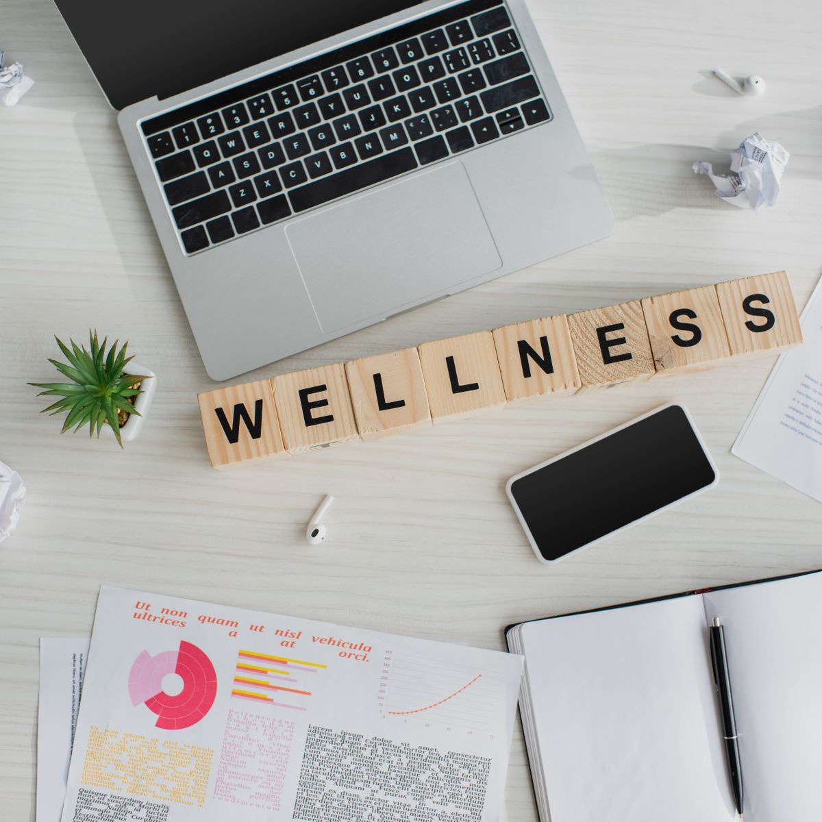 Desk with computer, papers, and blocks spelling &quot;wellness&quot; to represent Houston corporate wellness
